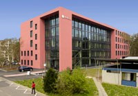 Eine Wissenschaftlerin und ein Wissenschaftler arbeiten hinter einer Glasfassade und mischen Chemikalien mit Großgeräten.